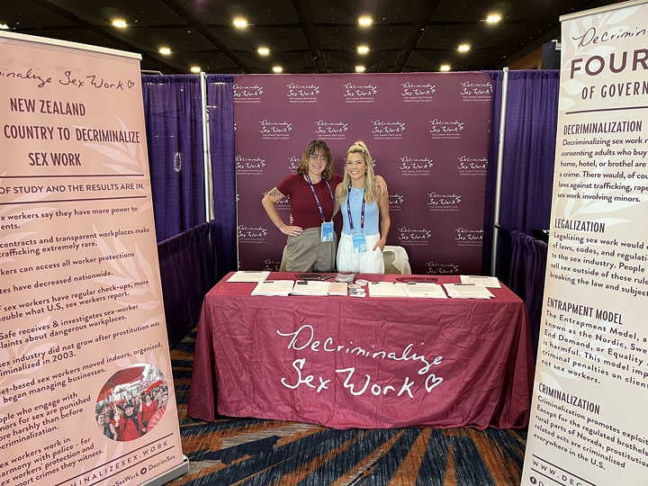 DSW Staff Attorney Becca Cleary and Development Manager Esmé Bengtson pose in front of Decriminalize Sex Work’s booth at FreedomFest.