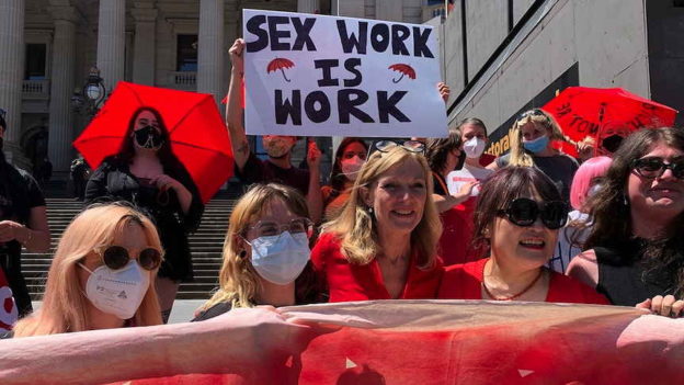 ​​MP Fiona Patten poses with sex workers and supporters of the decriminalization bill on the steps of parliament. (ABC News, 2022)